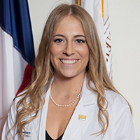 Woman with long, wavy, blonde hair wearing pearls and a white coat